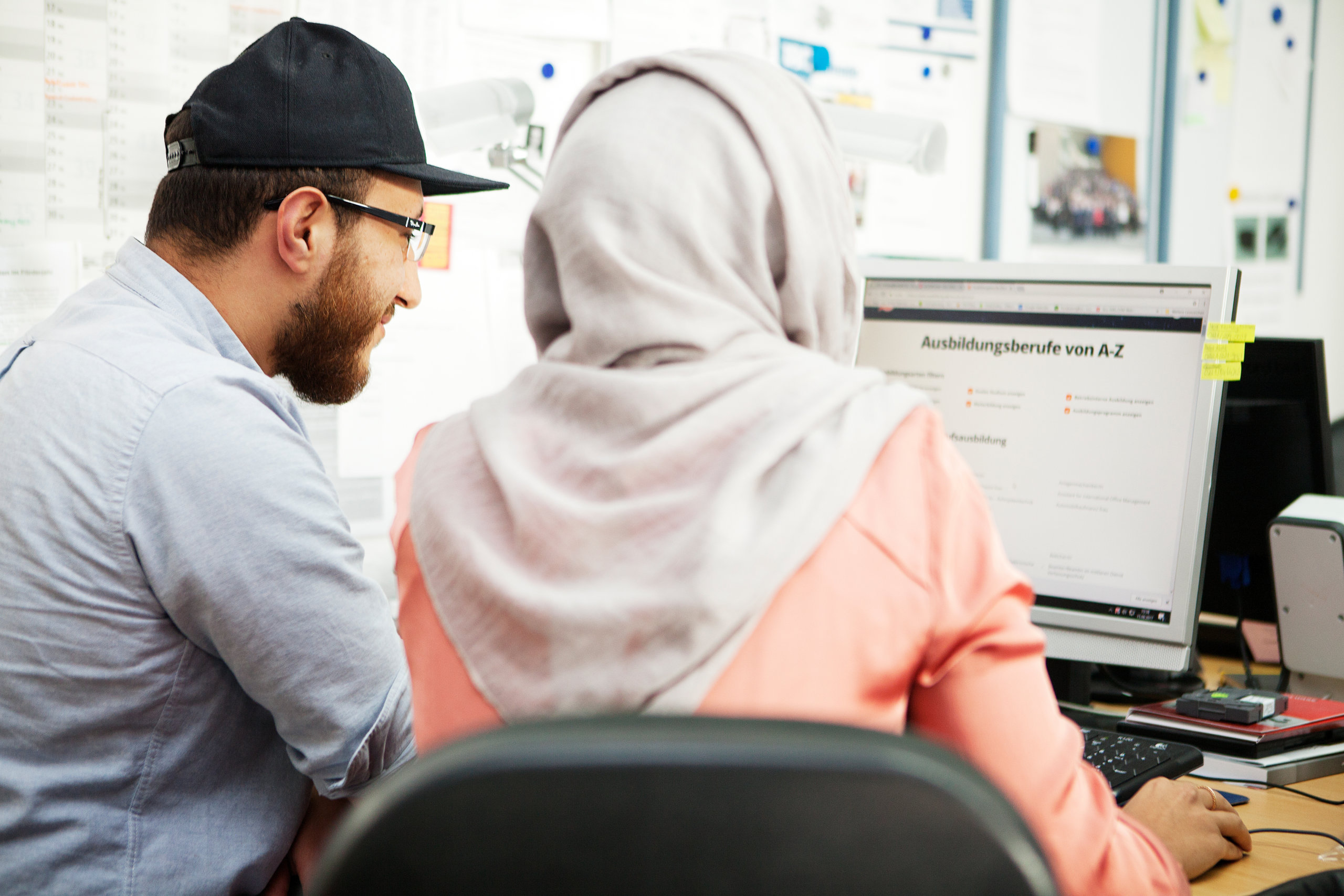 Junge Frau im Hijab sitzt mit jungem Mann vor Rechner